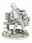 ESCULTURA, um (1) grupo escultórico confeccionado em faiança representando homem sentado em um banco com um cachorro, apresentando falhas na pintura, medindo 18x15,5cm.