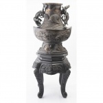 IMPORTANTE VASO ORIENTAL  BRONZE PATINADO COM RICAS FIGURAS MITOLÓGICAS SENDO DRAGÕES ORIENTAIS QUE AGARRAM A BORDA, O BOJO SUPERIOR APRESENTA UM MEDALHÃO CENTRAL COM AVE MITOLÓGICA EM ALTO RELEVO SOBRE FUNDO TEXTURIZADO O VASO REPUSA SOBRE UM APOIO EM MADEIRA ESCULPIDA EM RELEVO. ASSINADO NO VERSO MEDIDAS: 65 CM TOTAL PESO: 9 KILOS MEDIDA DO VASO: 34 CM