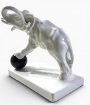 ESCULTURA REPRESENTANDO ELEFANTE  ESTILO ART'DECO EM PORCELANA BRANCA BRINCANDO COM UMA BOLA PRETA. MEDIDAS: 20 CM DE ALTURA / BASE 11 X  21 CM