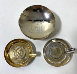 Três pelas em metal, sendo dois antigos cinzeiros com aplicação de moedas em relevo e um pratinho alto com gravação oriental . Medidas: maior 10 cm / menor 7 cm