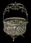 WMF  Antiga cesta em metal espessurado a prata, com recipiente em cristal encaixado, corpo ricamente vazado e ornamentado em alto-relevo com motivos de frutas, folhagens e laços, apoiado sobre quatro pés recurvos. Alça móvel com decoração em volutas, característica do refinado desenho Art Nouveau, evidenciando a qualidade da tradicional manufatura alemã WMF. Medidas: 10,5 x 12 x 16 cm.