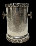 INAR (Argentina)  Antigo porta-garrafa (wine coaster) em metal espessurado a prata, reprodução do tradicional estilo Sheffield. Corpo cilíndrico ricamente gravado com arabescos, volutas e cartelas em fina decoração de inspiração vitoriana, com bordas superior e inferior ornamentadas em alto-relevo por folhas, flores e cachos de uva, apresentando alças laterais torneadas. Peça de elegante acabamento, marcada na base "Reprod. Sheffield  INAR  Rca. Argentina". Medidas: 15 x 13 x 17,5 cm.