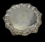 Antiga e imponente bandeja em metal espessurado a prata, de formato redondo, com borda recortada e contornada por concheados e volutas em relevo. Parte central finamente cinzelado com cartela rocaille envolta por arabescos e motivos florais. Medidas: 36 x 37,5 cm.