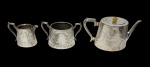 Sheffield  Conjunto com três peças em metal espessurado a prata, composto por bule, leiteira e açucareiro, de formato levemente abaulado, finamente cinzelados com motivos florais e folhagens, alças de desenho elegante e bico vertedor de linhas sinuosas. Manufatura marcada na base.  Medidas: 26 x 11 x 13,5 cm; 6,5 x 11 x 13 cm; 11,5 x 9 x 18 cm.