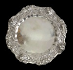 Antiga e imponente bandeja em metal espessurado a prata, de formato circular recortado, apoiada sobre quatro pés. Borda alta ricamente cinzelada com conchas, volutas e motivos vegetalistas em alto-relevo. Medidas: 5 x 45,5 cm.