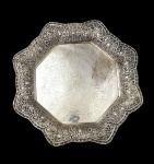 Grande e imponente bandeja em metal espessurado a prata, de formato octogonal recortado, com borda larga ricamente cinzelada em alto-relevo com volutas, flores e motivos vegetalistas. Centro finamente gravado com arabescos e folhagens, apresentando cartela central. Medidas: 4 x 40,5 x 40,5 cm