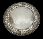 Imponente bandeja em metal espessurado a prata, de estilo Rococó, com centro ricamente gravado por motivos florais e cartelas, aba cinzelada com gomos e borda ornamentada em relevo com volutas e concheados. Apoiada sobre três pés. Medidas: 40,5 x 3,5 cm.