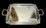 Antiga bandeja em metal espessurado a prata, de estilo neoclássico, formato retangular, com centro liso, borda gomada, cantoneiras ornamentadas por leques e alças laterais vazadas com o mesmo motivo decorativo. Medidas: 54,5 x 33 cm.