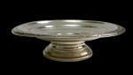 Antiga fruteira em metal espessurado a prata, de estilo neoclássico, com centro liso, borda ornamentada por frisos gravados e base circular torneada. Medidas: 6 x 23 cm.