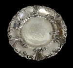 Antigo medalhão de parede em metal espessurado a prata, de estilo Art Nouveau, com centro gravado por motivo floral, borda recortada ricamente ornamentada em relevo com volutas, flores, folhagens e conchas estilizadas. Argola para fixação no verso. Medidas: 3 x 29,5 cm.