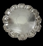 Antiga bandeja em metal espessurado a prata, de estilo Rococó, com centro ricamente gravado por arabescos e motivos florais, aba moldurada com gomos e borda recortada ornamentada em relevo por conchas e volutas. Medidas: 2,5 x 26 cm.