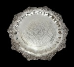 Antiga bandeja em metal espessurado a prata, de estilo Rococó, com centro finamente cinzelado por delicado padrão floral, aba moldurada com gomos e borda recortada ricamente ornamentada em relevo por rosas e folhagens. Apoiada sobre três pés. Medidas: 3 x 22,5 cm.