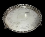 Antiga bandeja em metal espessurado a prata, de formato circular, com centro finamente gravado por motivos florais, galeria vazada ornamentada por folhagens em relevo e apoiada sobre três pés. Medidas: 5 x 26,5 cm.