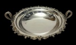 Antiga fruteira em metal espessurado a prata, de estilo Rococó, com corpo circular profundo, centro liso, borda recortada ricamente ornamentada em relevo por volutas, flores e folhagens, alças laterais em forma de cisnes e apoiada sobre três pés. Medidas: 8,5 x 38,5 x 32 cm.