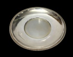 Antigo prato em metal espessurado a prata, com cavidade central e borda lisa ornamentada por friso perolado. Medidas: 19,5 cm de diâmetro.