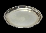 Antigo pratinho em metal espessurado a prata, de formato circular, com borda moldurada de contorno ondulado e centro liso. Medidas: 13,5 cm de diâmetro.