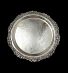 Antiga e imponente salva em metal espessurado a prata, de formato circular, com borda ricamente cinzelada em estilo Rococó, ornamentada por flores, conchas e volutas, centro finamente gravado com arabescos e motivos florais. Medidas: 3,5 x 40 cm.
