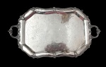 Antiga, imponente e gande bandeja em metal espessurado a prata, de formato retangular com cantos chanfrados, alças laterais vazadas, borda cinzelada em estilo Rococó com volutas e folhagens, centro finamente gravado com arabescos e motivos florais. Medidas: 3,5 x 62 x 36 cm.