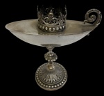 Antiga naveta sacra para incenso em metal espessurado a prata, com reservatório em formato naviforme elevado sobre pedestal, alça em voluta e suporte superior vazado, ricamente ornamentado com arabescos e elementos em relevo. Apresenta desgaste no banho de prata. Medidas: 20 x 7 x 18,5 cm.