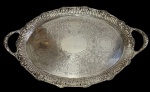 Antiga grande e imponente bandeja em metal espessurado a prata, de formato oval, com alças vazadas integradas, borda ricamente cinzelada em estilo Rococó, ornamentada por flores, folhagens e volutas em relevo, centro finamente gravado com arabescos, cartelas e motivos florais. Apresenta desgaste no banho de prata. Medidas: 36 x 57,5 cm.