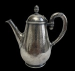 Antigo bule para café em metal espessurado a prata, marcado na base, com corpo em formato balaústre, decoração em cinzelado pontilhado, cartela central monogramada, bico e alça com frisos em relevo e tampa de encaixe com pomo torneado. Apresenta marcas do tempo. Medidas: 19 x 10 x 11 cm.