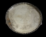 Antiga bandeja redonda em metal espessurado a prata, com borda vazada em padrão rendilhado e fundo ricamente cinzelado com decoração floral. Medidas: 3,5 x 29,5 cm.