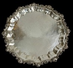 Antiga e imponente bandeja redonda em metal espessurado a prata, marcada, com borda recortada em relevo de inspiração rococó e centro ricamente cinzelado com decoração em arabescos. Medidas: 5 x 43 cm.