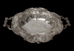 Antiga fruteira em metal espessurado a prata. Corpo oval recortado, borda ondulada e cinzelada, ricamente ornamentada em relevo com volutas, concheados e motivos vegetalistas, centro gravado e alças vazadas. Medidas: 7 x 39 x 25 cm.