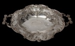 Antiga fruteira em metal espessurado a prata. Corpo oval recortado, borda ondulada e cinzelada, ricamente ornamentada em relevo com volutas, concheados e motivos vegetalistas, centro gravado e alças vazadas. Medidas: 7 x 39 x 25 cm.