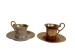 Conjunto com 2 xícaras para café com seus respectivos pires em porcelana esmaltada, decoradas com rica ornamentação em ouro, sendo uma em branco com padrão geométrico dourado e outra em tom vinho com motivos florais estilizados e filetes em ouro.