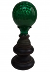 Antiga e imponente pinha decorativa em vidro verde, com bojo em relevo, montada sobre base torneada em madeira e metal. Apresenta trincados na região de encaixe do vidro junto à base, conforme fotografias. Medidas: 27 x 10 cm.