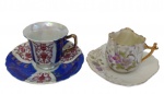 Duas xícaras para café em porcelana, decoradas em esmalte policromado, sendo uma com reservas em azul cobalto e ornamentação em vermelho sobre fundo branco, e outra com decoração floral em relevo, bordas onduladas e alça moldada. Ambas com frisos em ouro.