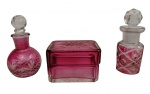 Três peças em cristal na tonalidade rosa, sendo dois pequenos perfumeiros com tampas lapidadas e uma caixinha retangular com tampa. Corpo lapidado e facetado. Medidas: caixinha 6,8 x 4,5 x 4,7 cm; perfumeiros 9 x 3,5 cm e 8,5 x 4 cm.