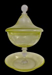 Saint-Louis, France. Antiga compoteira com tampa em cristal na tonalidade verde, ricamente gravada com motivos ornamentais. Corpo sobre haste e base circular, acompanhada de prato de apoio. Apresenta três bicados nas bordas do prato. Medidas: compoteira 27,5 x 15 cm; prato 18 cm.