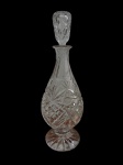 Antiga e imponente garrafa em cristal translúcido, com corpo ricamente lapidado em padrões geométricos, gargalo facetado, base estrelada e tampa lapidada. Medidas: 27 x 13 cm.