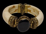 Bracelete em osso, composto por segmentos torneados, com aplicações em metal dourado trabalhado e fecho articulado, tendo ao centro cabochão em pedra negra. Medida: 8 cm de diâmetro.