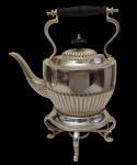 Antigo e imponente samovar em metal espessurado a prata, com corpo canelado, tampa com puxador em madeira torneada, alça basculante com empunhadura em madeira e base tripé vazada. Observação: ausência do fogareiro. Medidas: 30 x 22 x 12 cm.