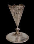 Antiga vaso solifleur em metal espessurado a prata, com corpo cônico ricamente gravado e vazado por decoração floral e folhagens, borda recortada e base circular. Medidas: 11,6 x 8,2 cm.