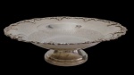 Fruteira em metal espessurado a prata, com centro ricamente gravado, borda recortada ornamentada em relevo com motivos de folhagens e flores, apoiada sobre base circular elevada. Medidas: 8 x 28,5 cm.