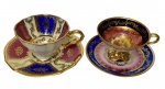 Duas xícaras de coleção para café em porcelana esmaltada e vitrificada, acompanhadas de seus respectivos pires, com rica decoração em reservas nos tons azul cobalto, vinho e marfim, ornamentação em arabescos e frisos dourados, sendo uma xícara com medalhão central representando cena galante.
