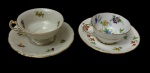 Duas xícaras de coleção para café em porcelana esmaltada e vitrificada, acompanhadas de seus respectivos pires. Uma manufatura KPM, com decoração floral policromada, corpo ornamentado em relevo e acabamento com frisos dourados; e uma manufatura inglesa, com decoração floral policromada e acabamento filetado a ouro. Manufatura no verso.