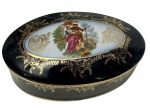 Antiga caixa em porcelana esmaltada e vitrificada, de formato oval, com tampa decorada por cena galante em reserva central, cercada por rica ornamentação dourada sobre fundo preto. Detalhes em dourado, manufatura na base. Medidas: 5,5 x 11,5 x 6,5 cm.