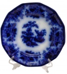 Antigo prato raso em porcelana inglesa "Flow Blue", marcado na base, com decoração em borrão, representando paisagem oriental, borda recortada e ornamentação em azul cobalto. Medidas: 24,3 cm de diâmetro.