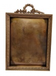 Antigo e imponente porta-retrato em metal dourado, ricamente cinzelado em relevo com frisos de folhagens e coroamento em guirlanda de louros entrelaçada, ladeada por motivos florais. Medidas: 29,3 x 20 x 2,4 cm.