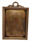 Antigo e imponente porta-retrato em metal dourado, ricamente cinzelado em relevo com frisos de folhagens e coroamento em guirlanda de louros entrelaçada, ladeada por motivos florais. Medidas: 29,3 x 20 x 2,4 cm.