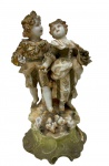 Antiga escultura em porcelana alemã da renomada manufatura de Sitzendorf, apresentando refinada pintura policromada com detalhes em ouro aplicados à mão, retratando casal de jovens camponeses em trajes românticos sobre base rochosa com pequenas aves, com a figura feminina carregando cesto de uvas e a masculina ofertando frutos, integrada sobre suntuosa base ornamental de estilo Rocaille que ostenta marcas de manufatura em subesmalte azul sob a base, numeração de pintor "109" e código de molde inciso na massa. Medidas: 16 x 8,5 x 8,5 cm.