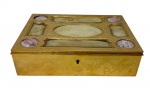 Antigo e sofisticado porta-joias de formato retangular, confeccionado em metal com requintado banho de ouro ricamente cinzelado na face frontal com guirlandas florais, laços e pontilhado, apresentando tampa abasculante ornamentada por trabalho que intercala placas geométricas com medalhões circulares de porcelana pintada à mão com motivos florais nos quatro cantos, peça dotada de fechadura frontal. Medidas: 6 x 23 x 17 cm.