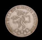 México. Moeda comemorativa de 25 Pesos, Jogos da XIX Olimpíada, México 1968, em prata, apresentando no anverso representação de atleta inspirada na arte pré-colombiana, acompanhada da inscrição "Juegos de la XIX Olimpiada México 1968" e dos anéis olímpicos. No reverso, brasão nacional dos Estados Unidos Mexicanos, com a águia sobre o cacto devorando a serpente, valor facial e legenda nacional. Peso: 22,5 g. Medidas: 3,8 cm de diâmetro.