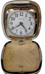 Relógio despertador de viagem Europa, fabricação alemã, com movimento mecânico de 2 rubis (2 Jewels), acondicionado em estojo rígido revestido, de formato quadrado com tampa articulada. Mostrador branco com algarismos arábicos e ponteiros luminescentes. Base marcada Germany, peça de coleção. Medidas: 7 x 8 x 3 cm.