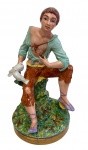 SUREDA, Espanha. Antiga e imponente escultura em porcelana esmaltada e policromada, representando jovem sentado sobre tronco, segurando duas pombas. Manufatura na base. Medidas: 34,5 x 18 cm.